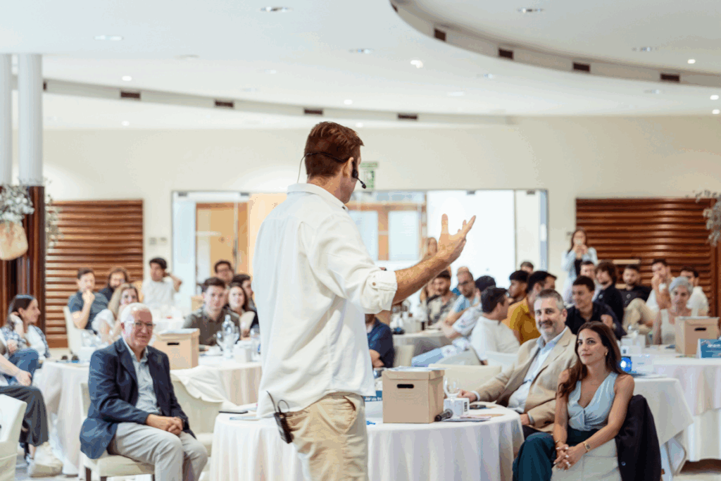 Ferran Tort imparte una charla a un público en mesas redondas durante un evento corporativo, visto desde atrás.