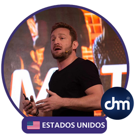 Fotografía de Andrea Iorio durante una conferencia, con micrófono de diadema y control remoto en mano, vestido de negro y frente a una pantalla iluminada, acompañado del distintivo de Estados Unidos y logotipo de CHM.