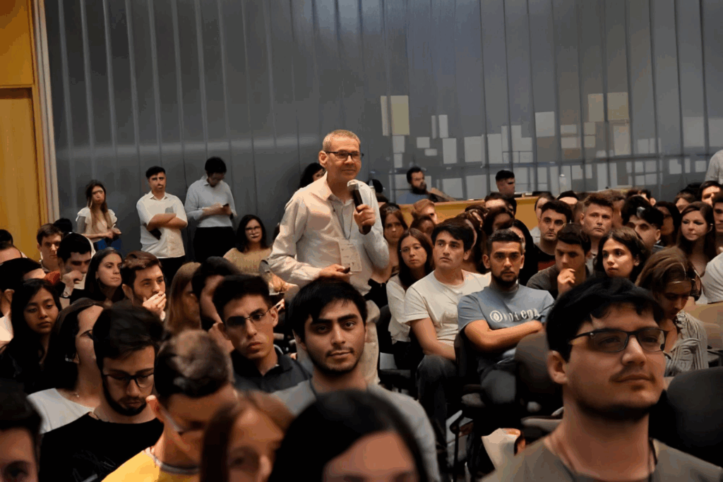 Fotografía de Daniel Colombo participando en una conferencia, de pie entre el público con un micrófono en mano, interactuando con una audiencia numerosa.