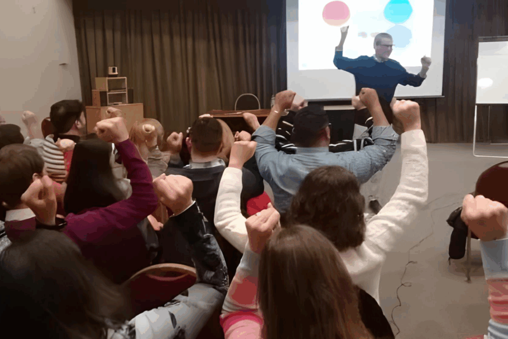 Fotografía de Daniel Colombo liderando un taller motivacional, frente a un grupo de participantes que levantan el puño en señal de entusiasmo y energía.