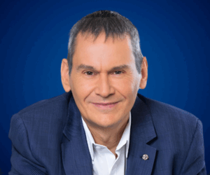 Fotografía de Daniel Colombo, sonriendo con traje azul marino y camisa blanca, frente a un fondo azul profesional.