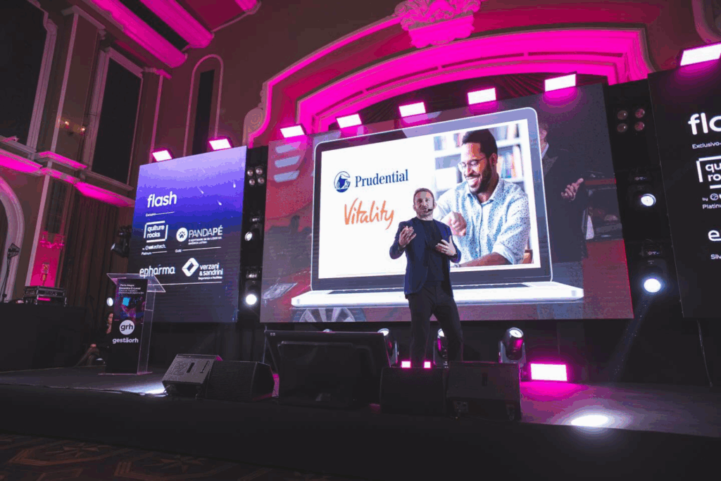 Fotografía de Andrea Iorio en una conferencia internacional, de pie sobre el escenario frente a una pantalla gigante con branding de Prudential y Vitality.