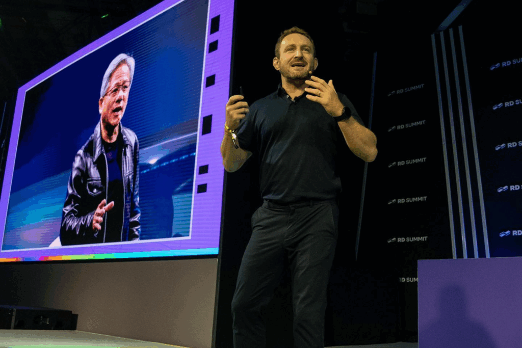 Fotografía de Andrea Iorio durante una conferencia en el RD Summit, de pie junto a una pantalla gigante con imagen de otro ponente, en un escenario iluminado profesionalmente.