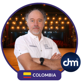Fotografía de Luis Miguel Trujillo, conferencista colombiano, de pie con los brazos cruzados, vistiendo camisa blanca con logotipos, sobre un fondo de escenario iluminado con luces cálidas, enmarcado con elementos gráficos de su país y marca.