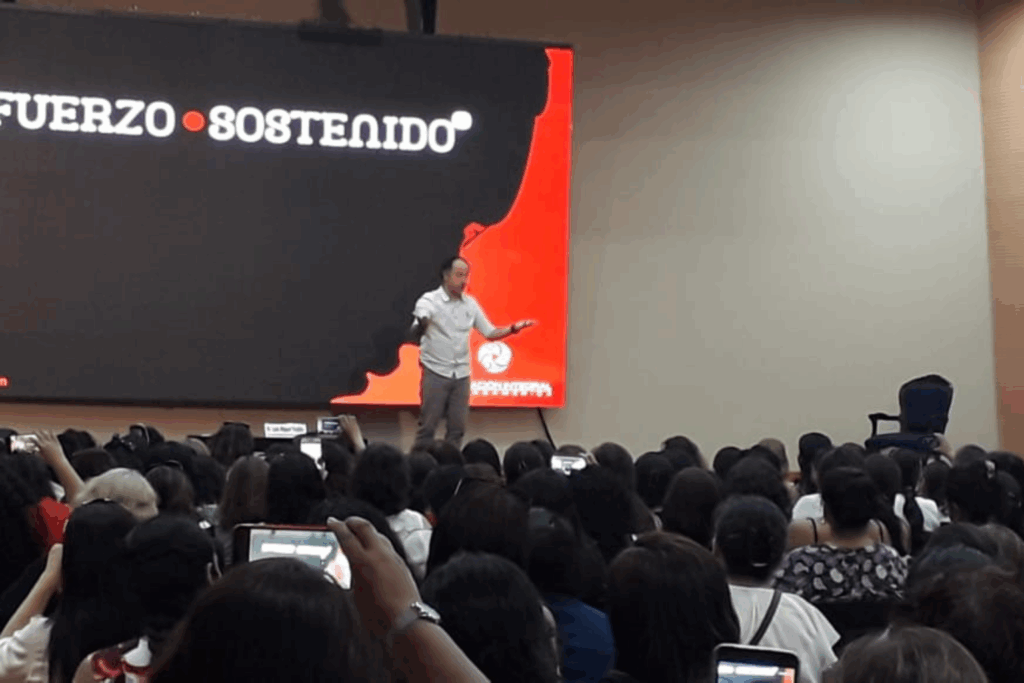 Fotografía de Luis Miguel Trujillo en el escenario durante una conferencia, frente a una audiencia numerosa, con una pantalla de fondo que muestra el mensaje “Esfuerzo sostenido”.