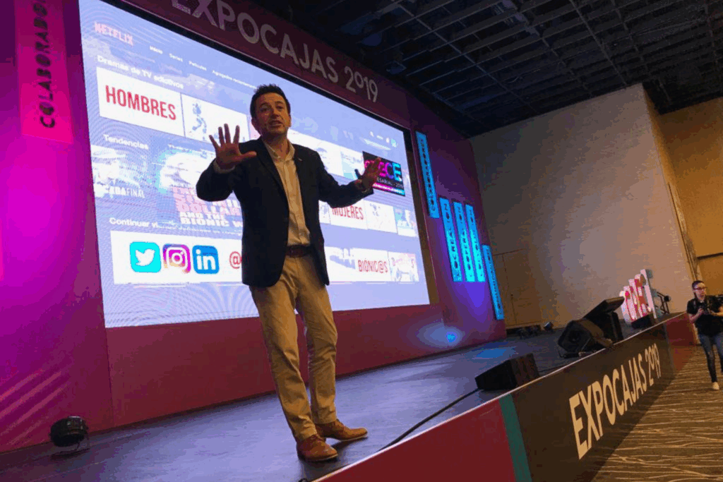 Fotografía de Rodrigo Saa durante una conferencia en Expocajas 2019, de pie sobre el escenario, gesticulando con energía frente a una gran pantalla digital.