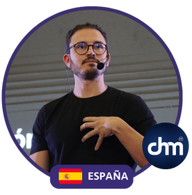 Fotografía de Borja Castelar durante una conferencia, con micrófono de diadema y camiseta negra, dentro de un marco circular con la bandera de España y el logotipo de CHM.