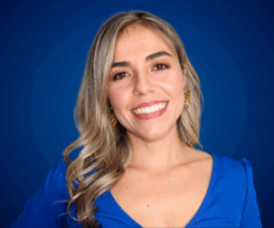 Retrato profesional de Yvonne Melina sobre fondo azul, con blusa azul y sonrisa cálida, transmitiendo confianza, alegría y profesionalismo.