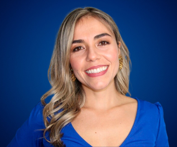 Retrato profesional de Yvonne Melina sobre fondo azul, con blusa azul y sonrisa cálida, transmitiendo confianza, alegría y profesionalismo.