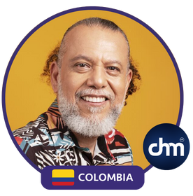 Fotografía de Alberto Linero, conferencista internacional de Colombia, con camisa estampada colorida y fondo amarillo vibrante, sonriendo con cercanía y calidez.
