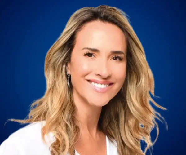 Angélica Castro, conferencista y coach de vida, sonriendo frente a un fondo azul.