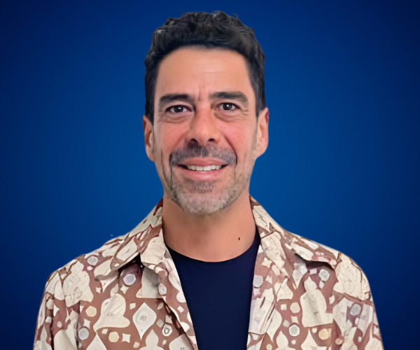 Fotografía de Gabriel Gurovich, sonriendo con una camisa estampada en tonos marrones y camiseta negra, sobre un fondo azul profesional.