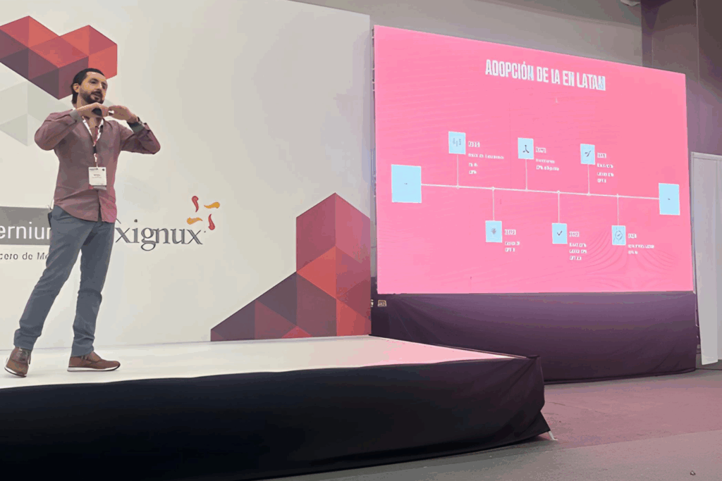 Fotografía de Daniel Villarreal impartiendo una conferencia sobre la adopción de la inteligencia artificial en Latinoamérica, acompañado de una presentación proyectada en pantalla.