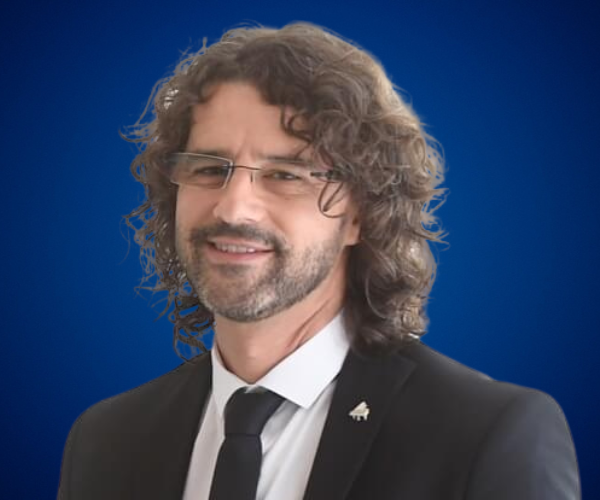 Antoni Tolmos, pianista y conferencista, con traje formal y gafas, fondo azul.
