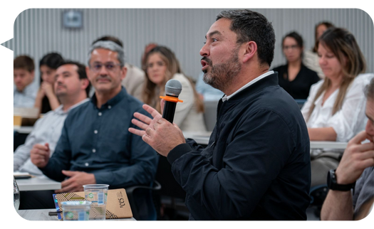 Claudio López Moreno participando en una sesión interactiva, haciendo uso del micrófono para compartir sus ideas con los asistentes en una sala de conferencias.