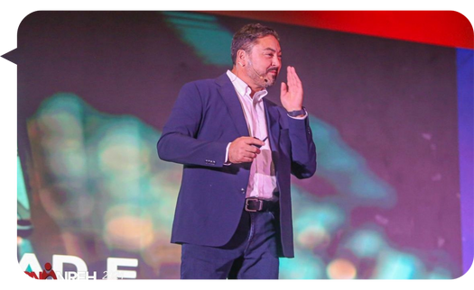 Claudio López Moreno en el escenario de una conferencia, gesticulando para enfatizar su mensaje mientras conecta con la audiencia.