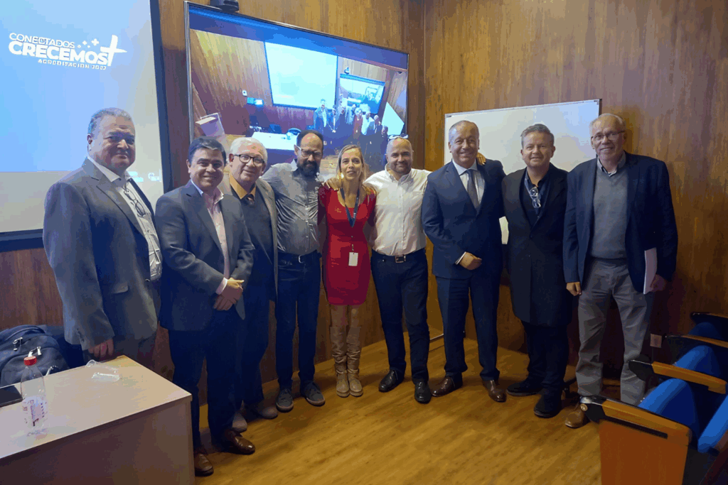 Fotografía de Fernando Veliz junto a un grupo de profesionales en un evento corporativo, posando sonrientes en un auditorio con pantalla de proyección.
