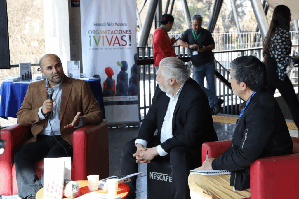 Fotografía de Fernando Veliz en una charla-coloquio junto a otros profesionales, sosteniendo un micrófono mientras conversa sobre liderazgo organizacional.