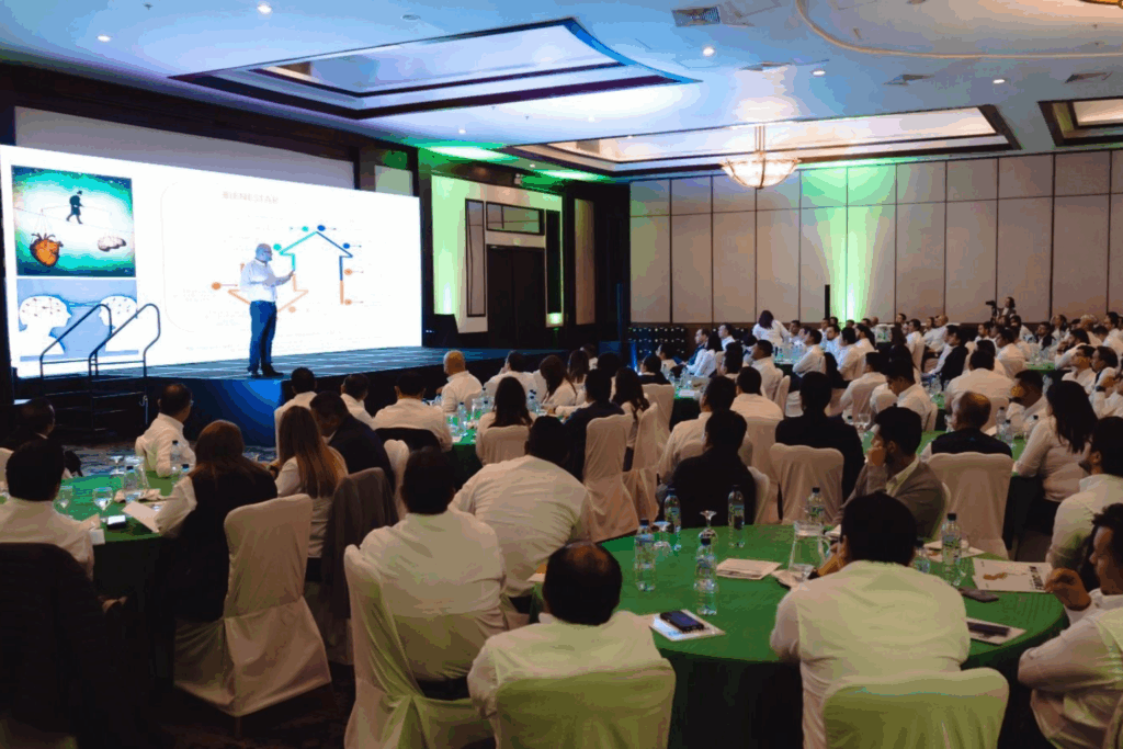 Fotografía de Fernando Veliz durante una conferencia empresarial, de pie en un escenario iluminado, frente a una audiencia atenta en un salón elegante.
