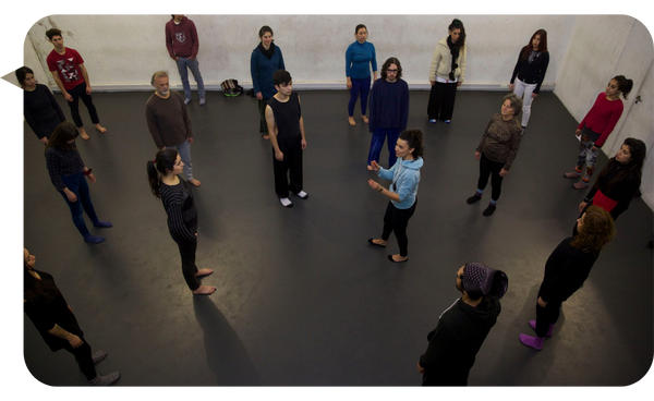 Cristina Fuentes dirigiendo un taller de teatro y mindfulness, con los participantes formando un círculo a su alrededor en un espacio amplio.