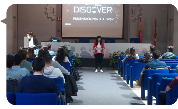 Marta Freire conduciendo un taller sobre presentaciones efectivas, de pie frente a una audiencia en una sala de conferencias, con una pantalla de presentación detrás de ella.