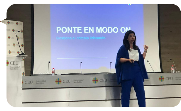 Marta Freire presentando "Ponte en Modo ON" en la Universidad CEU San Pablo, vistiendo un conjunto azul, hablando frente a una pantalla con el título de la conferencia.