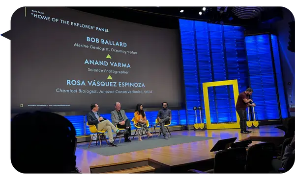 Dra. Rosa Vásquez Espinoza en el panel "Home of the Explorer" junto a Bob Ballard y Anand Varma, en un auditorio con fondo azul y amarillo.