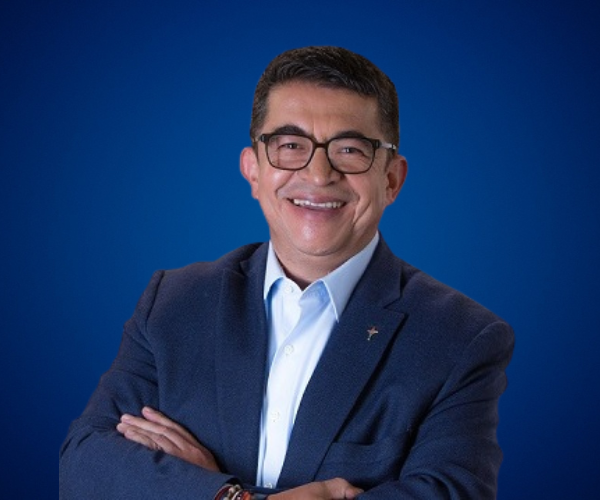 Diego Tovar con gafas y chaqueta oscura sonriendo en fondo azul.