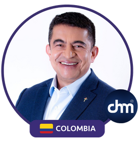 Diego Tovar con chaqueta azul sonriendo con un fondo blanco y bandera de Colombia.