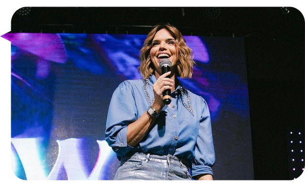 Rashel Díaz, conferencista y coach motivacional, hablando en el escenario con un micrófono en la mano y una sonrisa radiante, inspirando a su audiencia con su mensaje de empoderamiento.