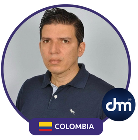 Juan Carlos Mojica con camiseta polo azul y fondo gris, con un borde circular que incluye una bandera de Colombia y el logo de CHM.