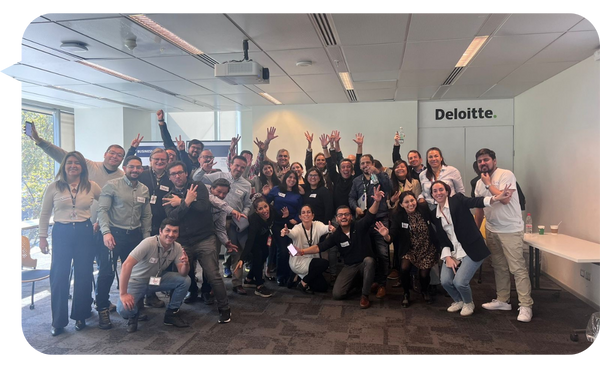 Un grupo de personas sonrientes y levantando las manos durante una sesión de formación dirigida por Julián Mendiola en una sala de conferencias de Deloitte.