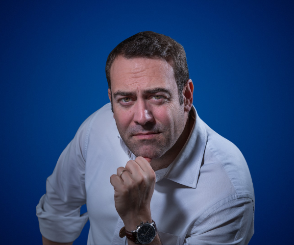 Nacho Barraquer con camisa blanca, en pose pensativa, sobre un fondo azul.