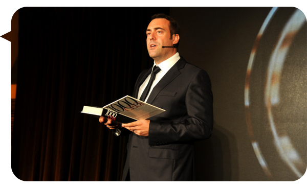 Nacho Barraquer sosteniendo un libro mientras habla en un escenario.