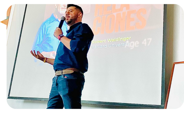 Juan Carlos Gutiérrez dando una conferencia sobre relaciones humanas con una presentación de fondo en un evento.