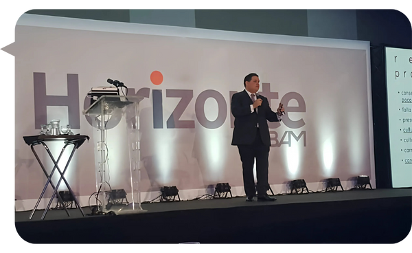 Leo Rodríguez de pie en un escenario, vestido de traje oscuro, presentando en un evento llamado "Horizonte BAM", con un micrófono en mano.