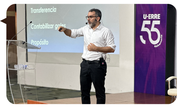 Martín Quirós dando una conferencia en U-ERRE sobre gestión empresarial y liderazgo, con gráficos proyectados al fondo.