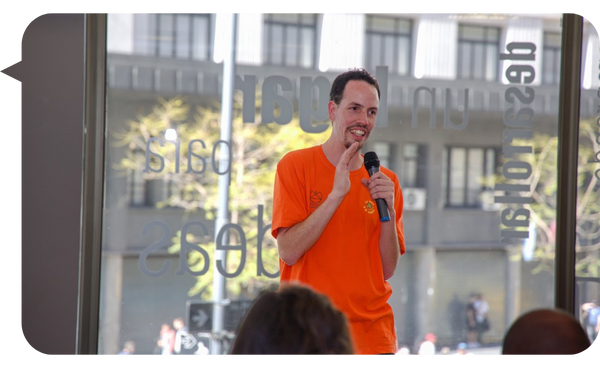 Mataco Iglesias hablando en una conferencia con vista urbana de fondo.