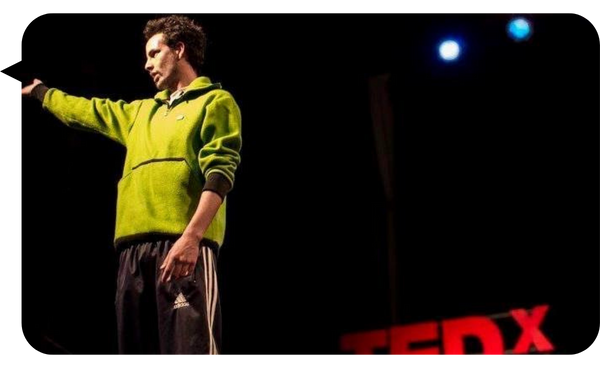 Mataco Iglesias dando una charla TEDx en el escenario con sudadera verde.