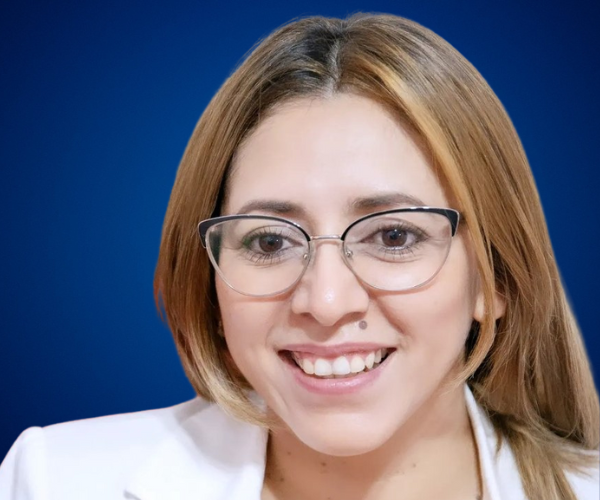 Retrato de Rita Vieyra, psicóloga organizacional y conferencista internacional, sonriendo con un fondo azul.