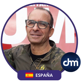 Hombre con gafas, chaqueta militar y fondo rojo con bandera de España.