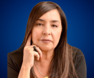 Retrato de Mayte Ariza con fondo azul, luciendo una expresión pensativa y una mano apoyada en su rostro.