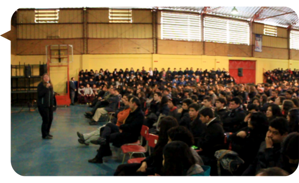 Sylvia Langford dando una conferencia en un gimnasio lleno de estudiantes y adultos.