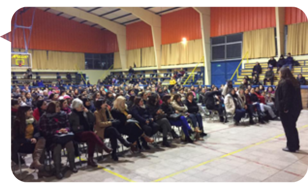 Sylvia Langford hablando frente a una gran audiencia en un gimnasio escolar.