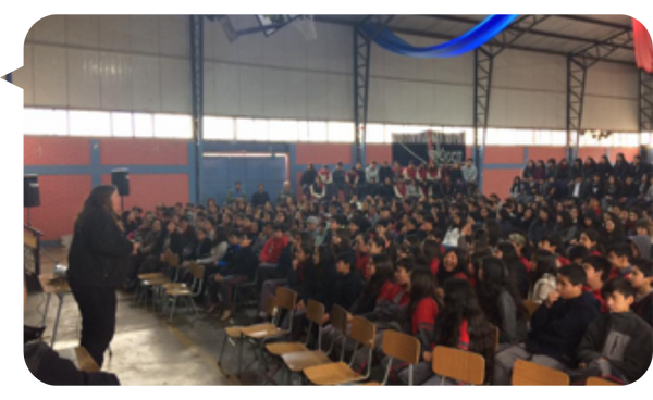 Sylvia Langford dando una conferencia ante un grupo numeroso de estudiantes en un gimnasio escolar.