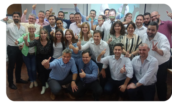 Alejandro Delobelle posando con un grupo grande de profesionales al finalizar una sesión de capacitación, todos sonrientes y mostrando gestos de aprobación.