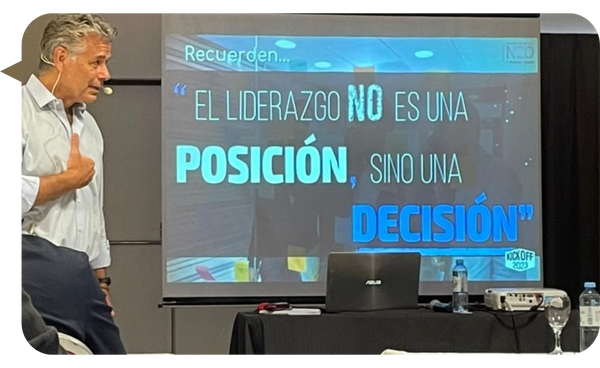 Alejandro Delobelle impartiendo una conferencia sobre liderazgo, frente a una pantalla que muestra la frase: "El liderazgo no es una posición, sino una decisión".