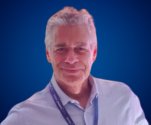 Retrato de Alejandro Delobelle, conferencista internacional, vistiendo una camisa clara con un fondo azul, sonriendo de manera carismática.