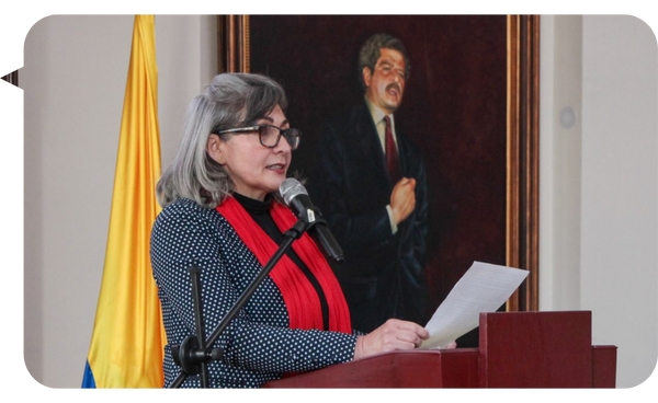 Beatriz Ramírez, conferencista, ofreciendo un discurso en un podio con una bandera de Colombia de fondo.