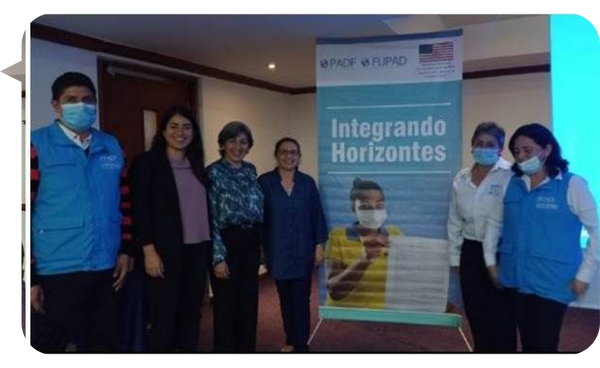 Beatriz Ramírez junto a un grupo de personas en un evento de la iniciativa "Integrando Horizontes", con un cartel informativo de fondo.